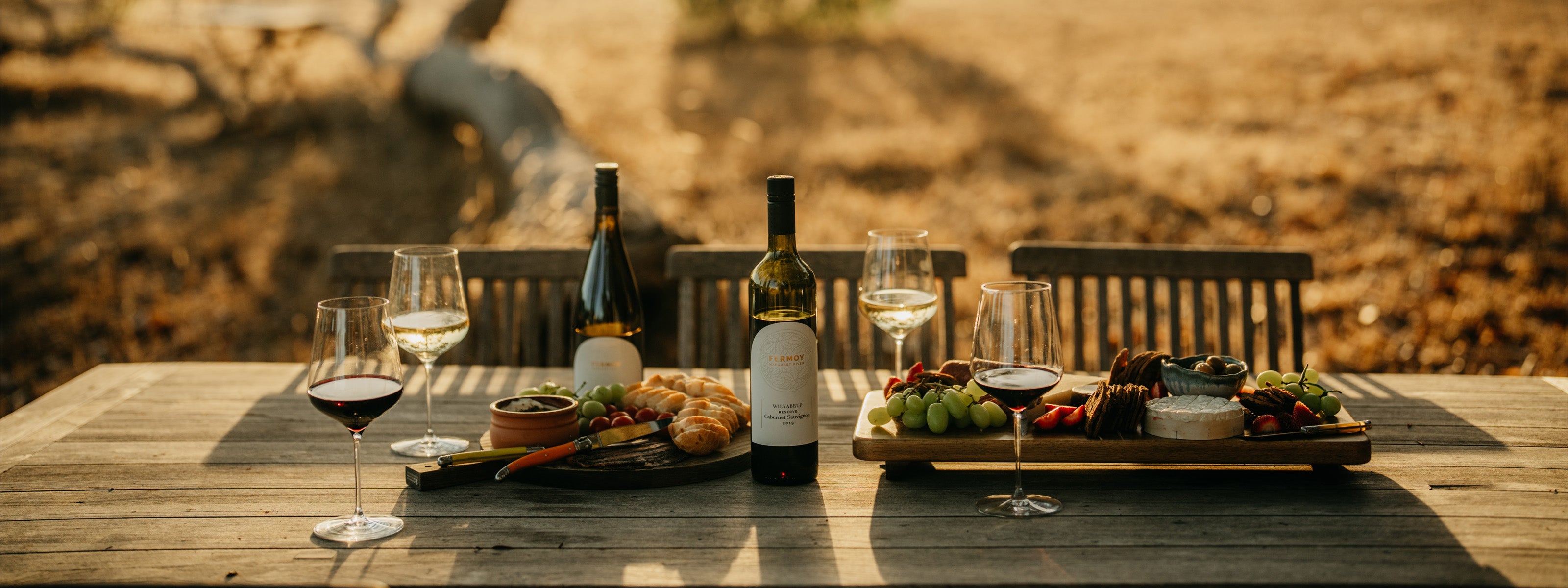 Selection of Fermoy Estate wines displayed on a rustic outdoor table, surrounded by natural vineyard light.